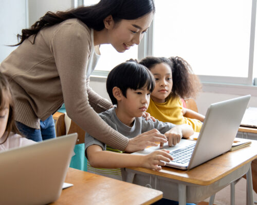 An Asian female teacher teaches primary school students to use computers and tablets to search for knowledge and information through the Internet. Classroom diversity students. Back to school concept